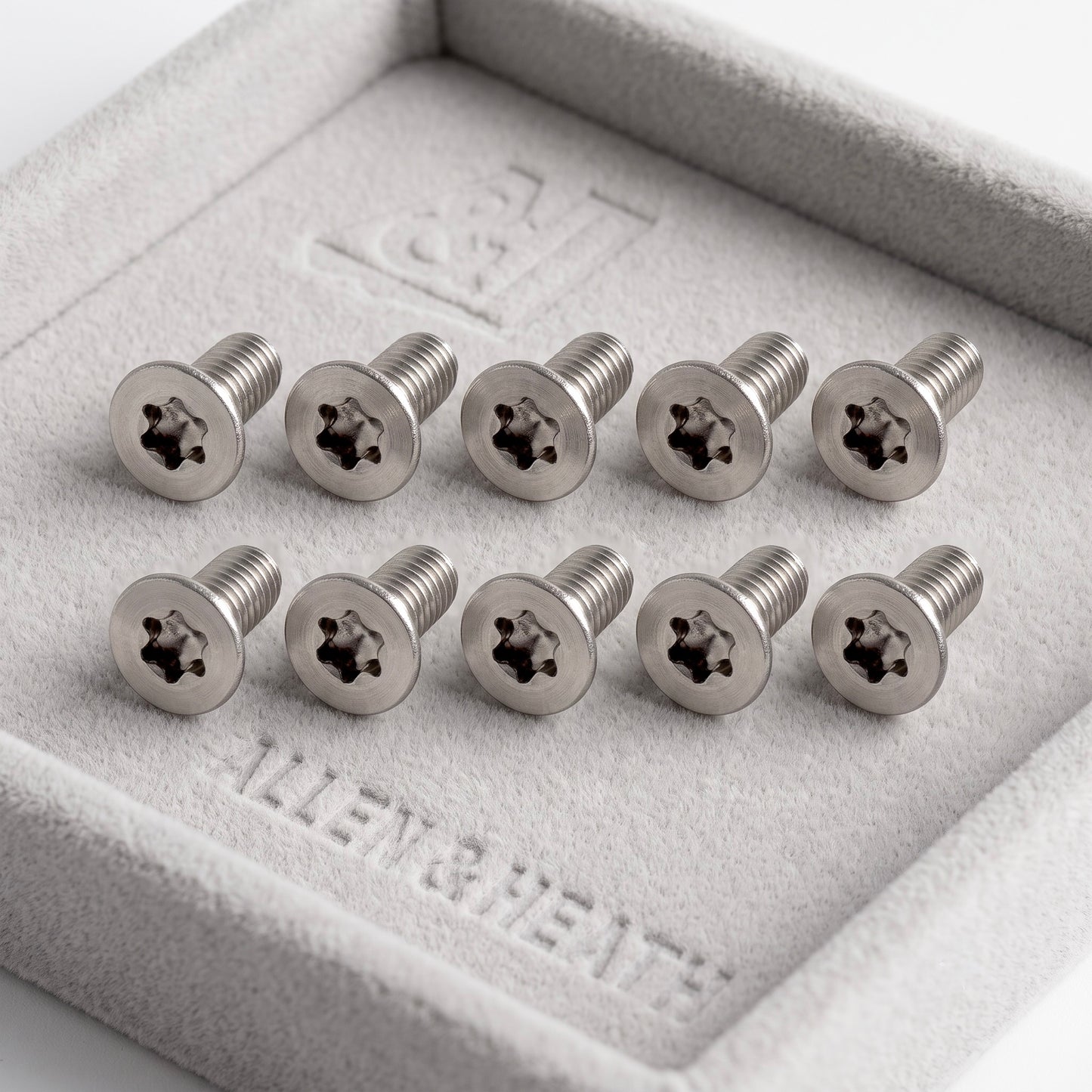 Ten silver Allen & Heath star-drive screws arranged in two rows inside a gray felt jewelry box.