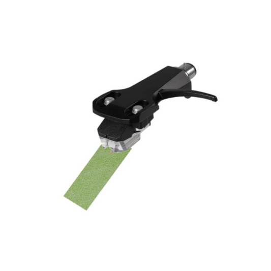 A high-angle studio shot against a plain white background shows a black phono cartridge mounted on a headshell, with its needle resting on a small, rectangular strip of light green abrasive paper, known as "Linn Green Paper." The cartridge is angled toward the lower left, and the fine green paper is positioned diagonally beneath the stylus tip to demonstrate a specialized cleaning method for turntable needles.