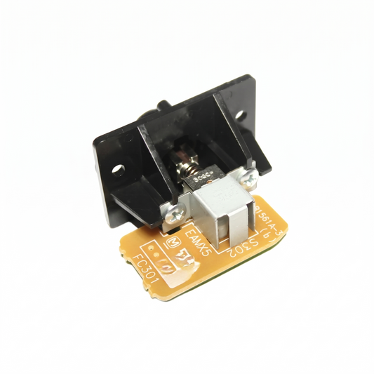 A close-up studio shot against a seamless white background showing the rear side of a Technics reset button assembly. The unit features a black plastic mounting bracket attached via two silver screws to a small, light-brown printed circuit board (PCB).