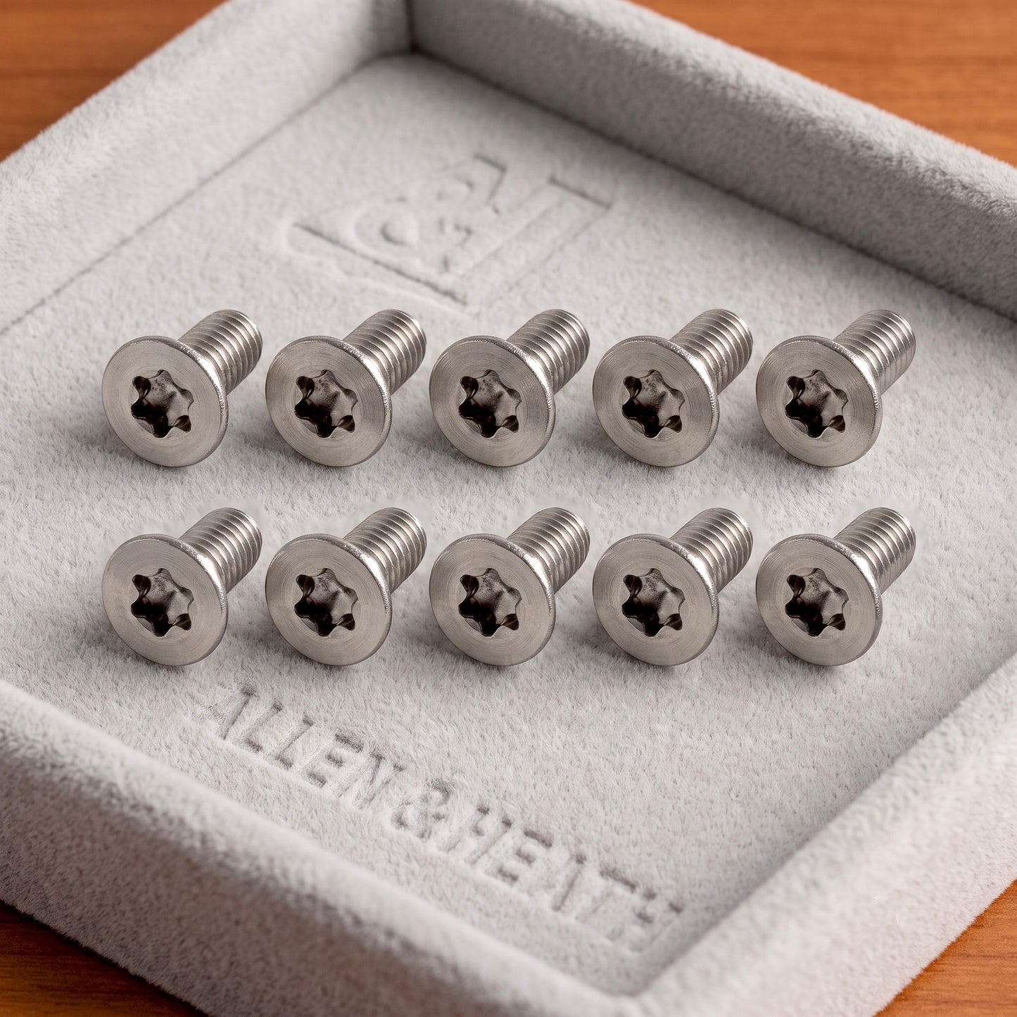Ten silver Allen & Heath star-drive screws arranged in two rows inside a light gray textured presentation box on a wooden surface.