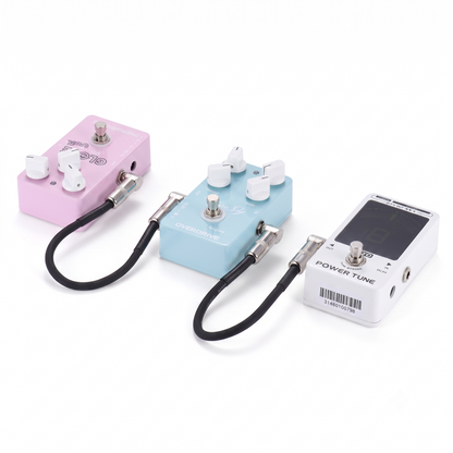 Two black Ammoon AC-10 guitar patch cables shown in use, linking three different stompbox effects pedals (pink, light blue overdrive, and white tuner) together on a clean white background.