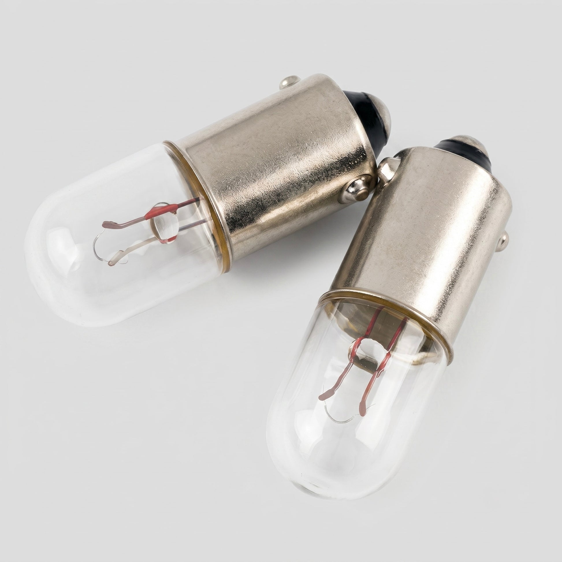 Two vintage-style T47 miniature pilot light bulbs with cylindrical clear glass envelopes, showing the internal wire filaments and supports, paired with metal bayonet bases and set against a solid white background.