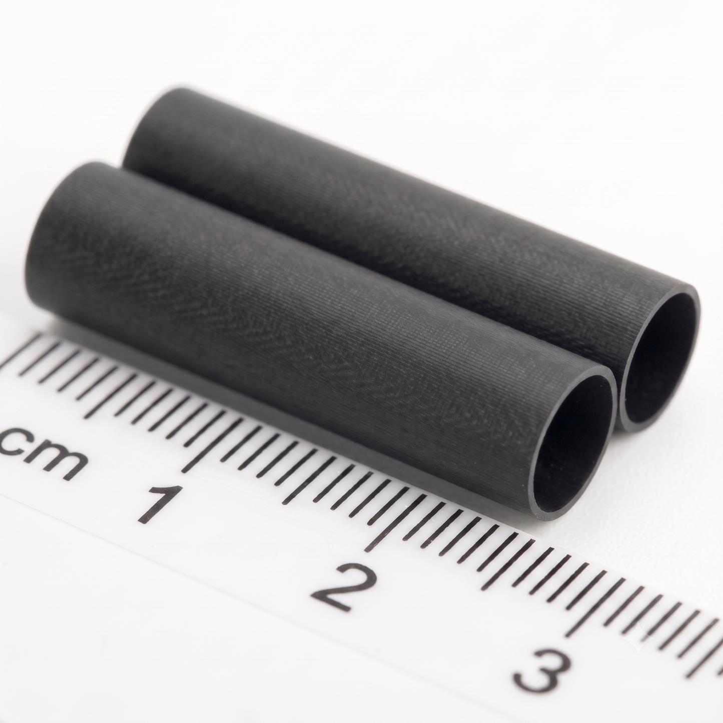 Two small black cylindrical tube with a textured surface, shown diagonally next to a white ruler with centimetre markings to indicate its size.