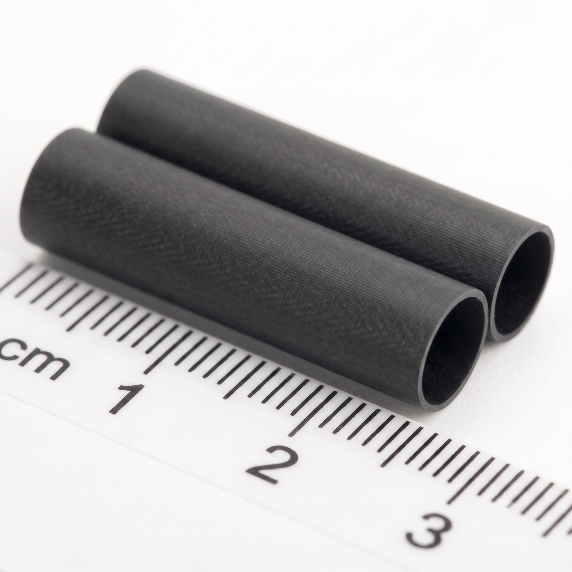 Two small black cylindrical tube with a textured surface, shown diagonally next to a white ruler with centimetre markings to indicate its size.