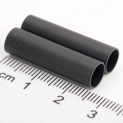 Two small black cylindrical tube with a textured surface, shown diagonally next to a white ruler with centimetre markings to indicate its size.