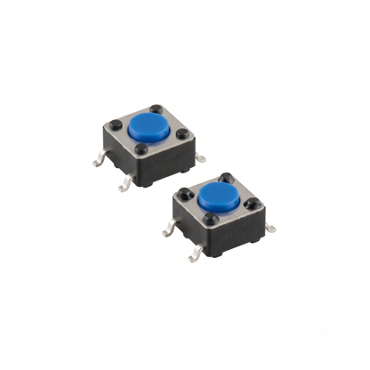 An isolated studio shot of a two-pack of upgraded power switches for a Gtech handheld vacuum, arranged diagonally against a seamless white background. Each component is a small, square tactile micro-switch featuring a black plastic housing body, a metallic silver top plate secured by four tiny rivets, and a vibrant blue circular push-button in the centre. Four gull-wing-shaped metallic solder leads extend from the sides for surface-mount installation.
