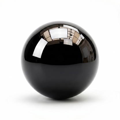 A glossy, highly reflective black ceramic ball bearing centered against a pure white background, showing a distorted reflection of an interior room on its upper surface.