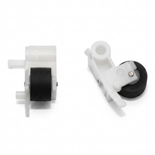 Two identical pinch roller assemblies from different angles, set against a seamless white background. On the left: The assembly is positioned vertically, showing its profile. It features a textured, black rubber cylindrical roller mounted inside a molded white plastic housing. Small plastic pins and tabs extend from the left side of the casing. On the right: The second assembly is angled diagonally, providing a top-down view of its mechanism. It highlights a prominent circular plastic pivot hole at the top,