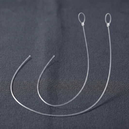 A close-up photograph featuring two identical, replacement anti-skate threads for a turntable, presented as a 2-pack. Both translucent, ultra-thin monofilament nylon lines are arranged side-by-side in parallel, semi-circular curves on a dark grey, textured fabric background. Each line is identically sized, cleanly cut at one open end on the left, and features a pre-tied loop secured with a small, precise knot at the top right.