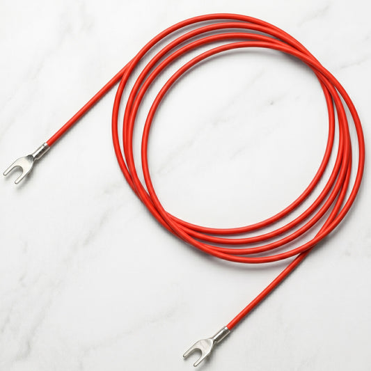 A bright red turntable earthing ground lead cable arranged in a loose, circular coil over a smooth, white marble background with subtle grey veining. Both ends of the flexible, smooth-textured red cable extend outward, terminating in polished coloured spade connector forks with visible metallic crimp sleeves.