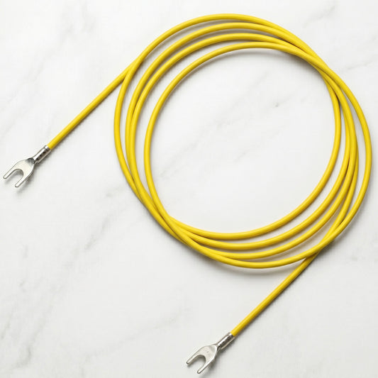 An overhead product shot of a bright yellow, single-core turntable ground wire, shown coiled on a light grey and white marble surface, features two pre-terminated silver spade/fork connectors, identical to the cable in "Pro-Ject Turntable Earthing Ground Lead (Yellow) By Perform.