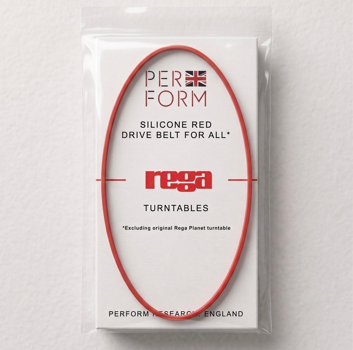 Front view of a "Perform" brand replacement turntable belt. A thin, circular red silicone belt is stretched into an oval shape over a white rectangular card inside a clear plastic packet. The card features text that reads: "PERFORM" with a small Union Jack icon, "SILICONE RED DRIVE BELT FOR ALL* REGA TURNTABLES", and a small note at the bottom stating "*Excluding original Rega Planet turntable". The bottom of the card reads "PERFORM RESEARCH, ENGLAND".