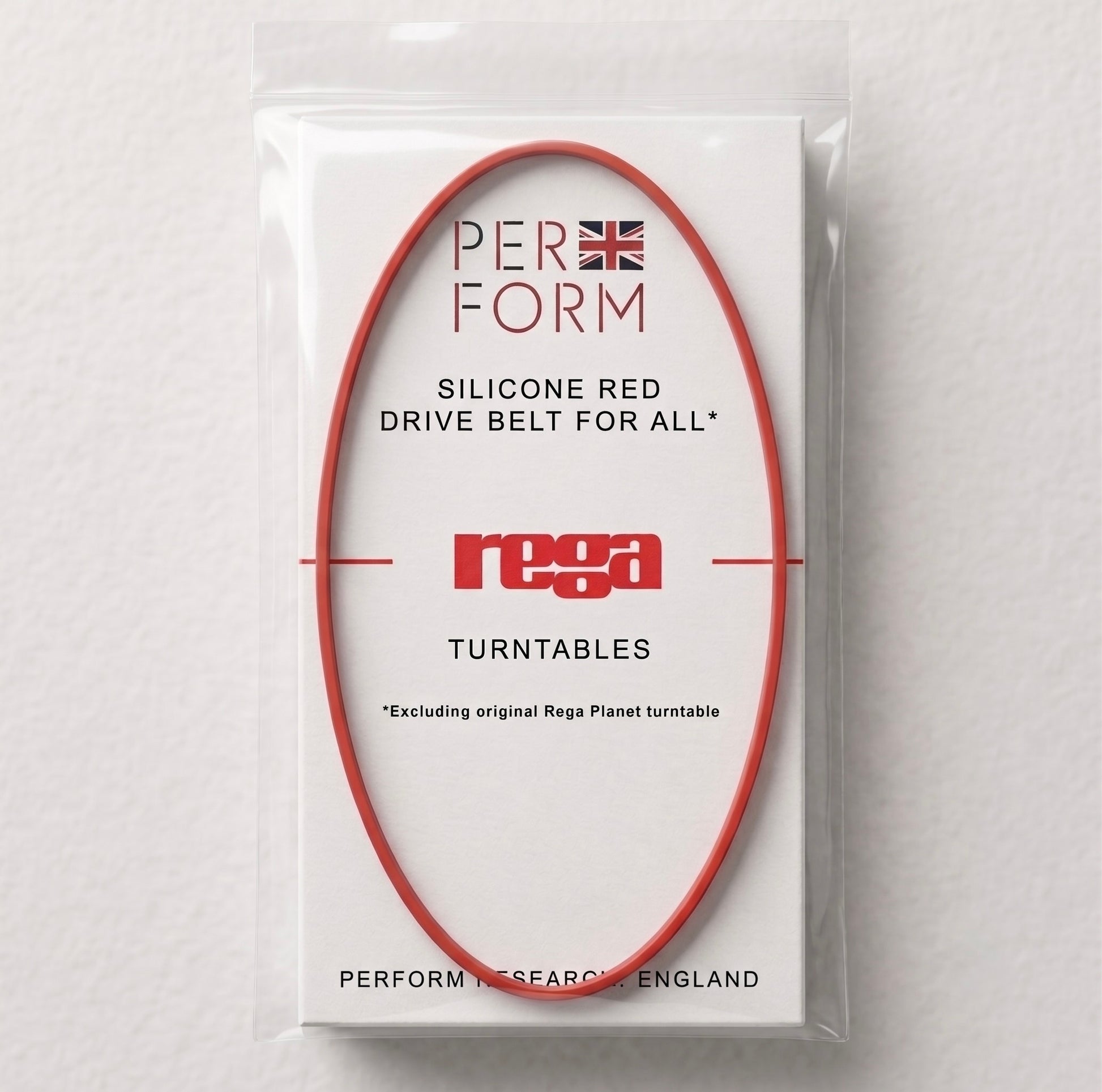Front view of a "Perform" brand replacement turntable belt. A thin, circular red silicone belt is stretched into an oval shape over a white rectangular card inside a clear plastic packet. The card features text that reads: "PERFORM" with a small Union Jack icon, "SILICONE RED DRIVE BELT FOR ALL* REGA TURNTABLES", and a small note at the bottom stating "*Excluding original Rega Planet turntable". The bottom of the card reads "PERFORM RESEARCH, ENGLAND".
