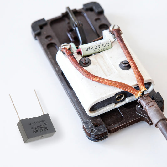 An electronic component assembly featuring a white plastic housing with copper-colored wires, a small cylindrical capacitor, and a separate black rectangular relay or transistor part on a plain white background.