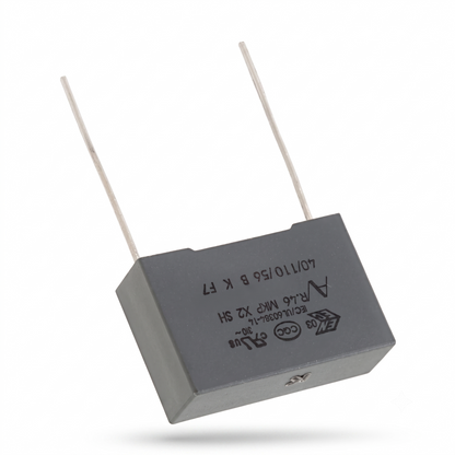 A gray rectangular electronic capacitor with two thin metal leads, shown at an angle on a white background with a soft shadow.