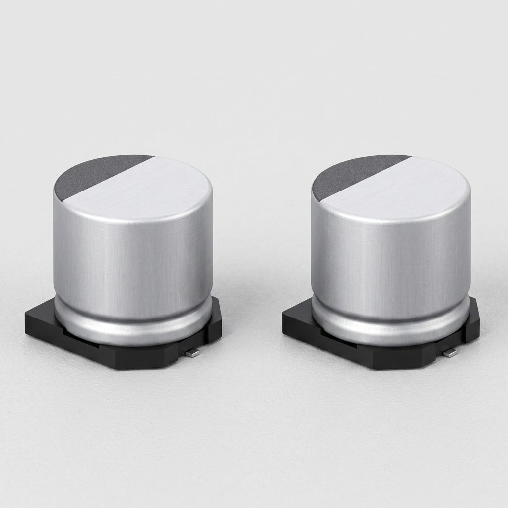 high-resolution, clean product shot of two identical surface-mount (SMD) electrolytic capacitors side by side against a neutral, light-gray background. Each capacitor features a cylindrical silver aluminum body sitting on a black plastic base with small metal soldering leads protruding from the bottom. The flat circular tops of the capacitors are divided into a smooth silver section and a textured, dark gray semi-circular marking indicating polarity. The image is crisp, showing fine metallic brushed texture