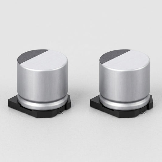 high-resolution, clean product shot of two identical surface-mount (SMD) electrolytic capacitors side by side against a neutral, light-gray background. Each capacitor features a cylindrical silver aluminum body sitting on a black plastic base with small metal soldering leads protruding from the bottom. The flat circular tops of the capacitors are divided into a smooth silver section and a textured, dark gray semi-circular marking indicating polarity. The image is crisp, showing fine metallic brushed texture