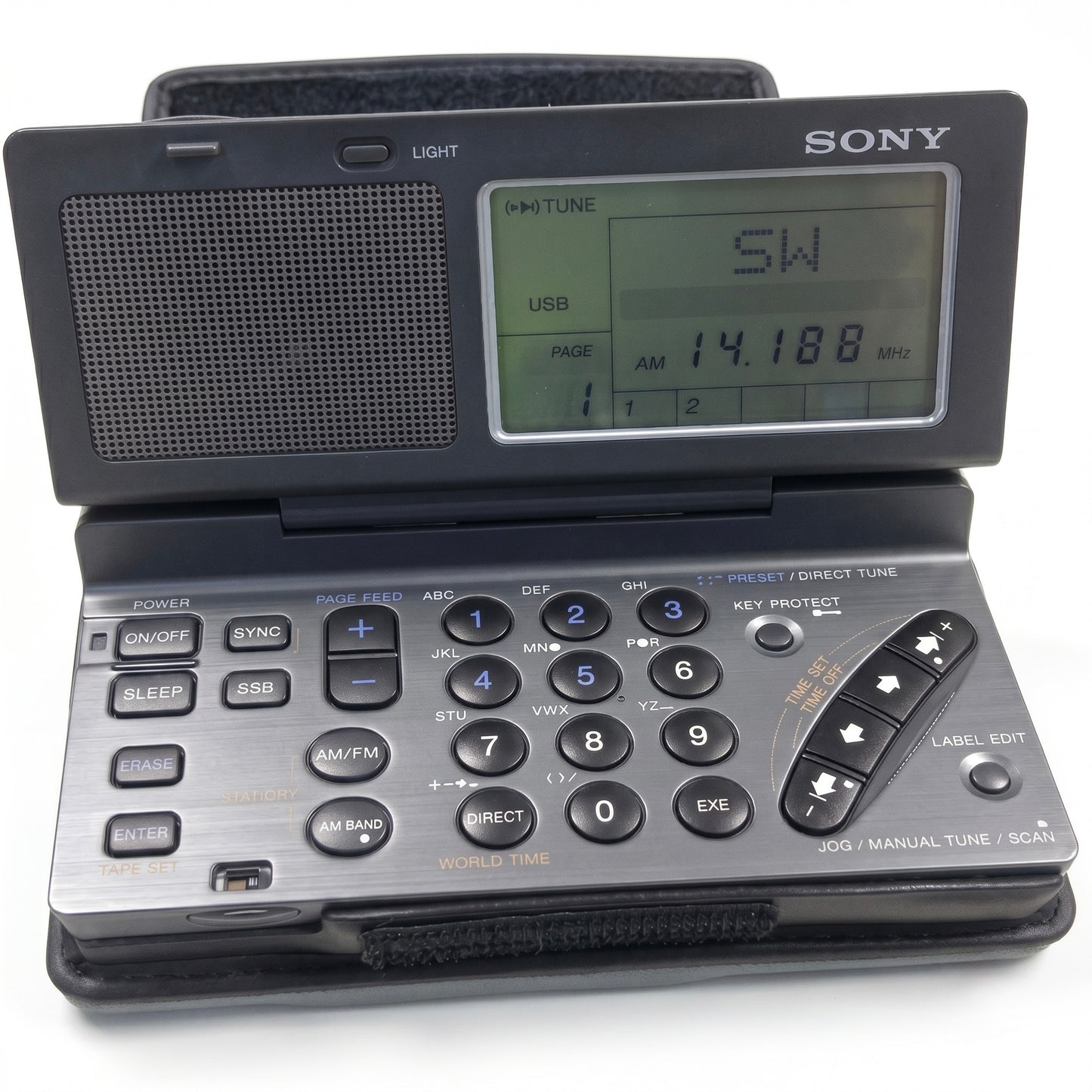 An open Sony ICF-SW100 multi-band world band shortwave receiver radio, resting in its black leather case on a white background. The device is open like a small notebook, showing a large speaker grille on the left and a detailed LCD screen on the right of the top section, which displays tuning information: