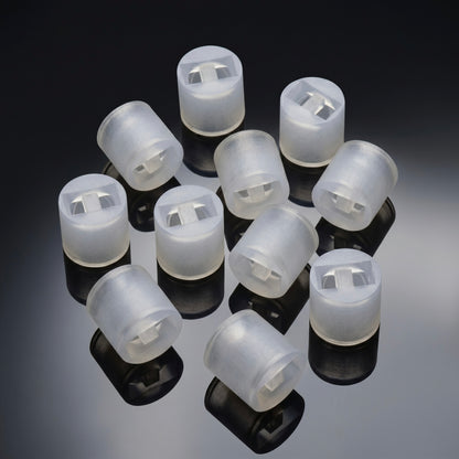 close-up studio shot of ten identical, small cylindrical spacers arranged together on a glossy, reflective dark grey surface. The spacers are made of a translucent, frosted white plastic or silicone material. Each piece features a hollow interior with a rectangular cutout and a small central dividing tab. Clear, dark reflections of each cylinder are cast directly beneath them on the shiny surface.