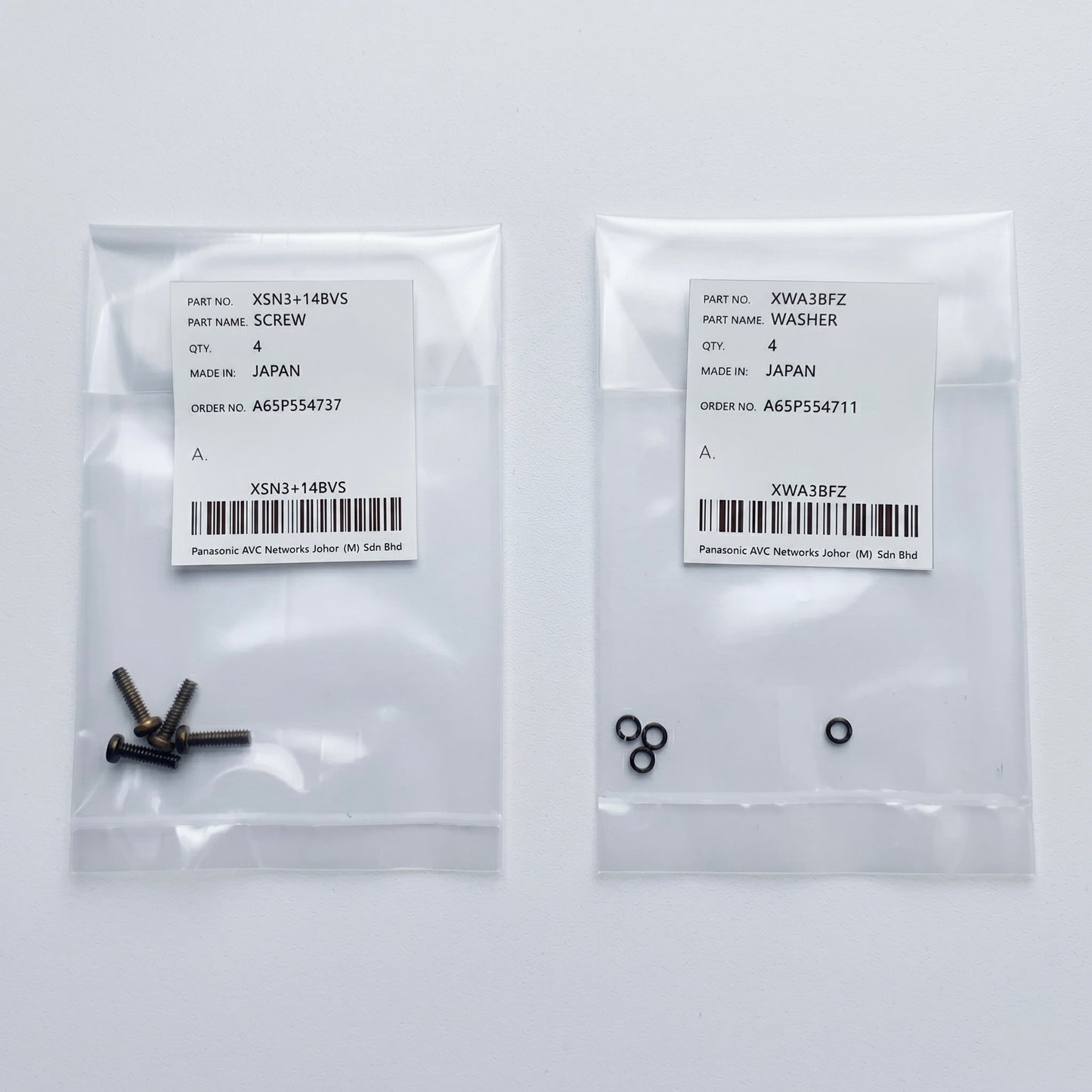 Two clear plastic parts bags side-by-side on a white surface. The left bag contains four small dark metal screws with a white label marked part number XSN3+14BVS. The right bag contains four small black locking washers with a white label marked part number XWA3BFZ. Both labels indicate they are genuine Panasonic parts made in Japan.