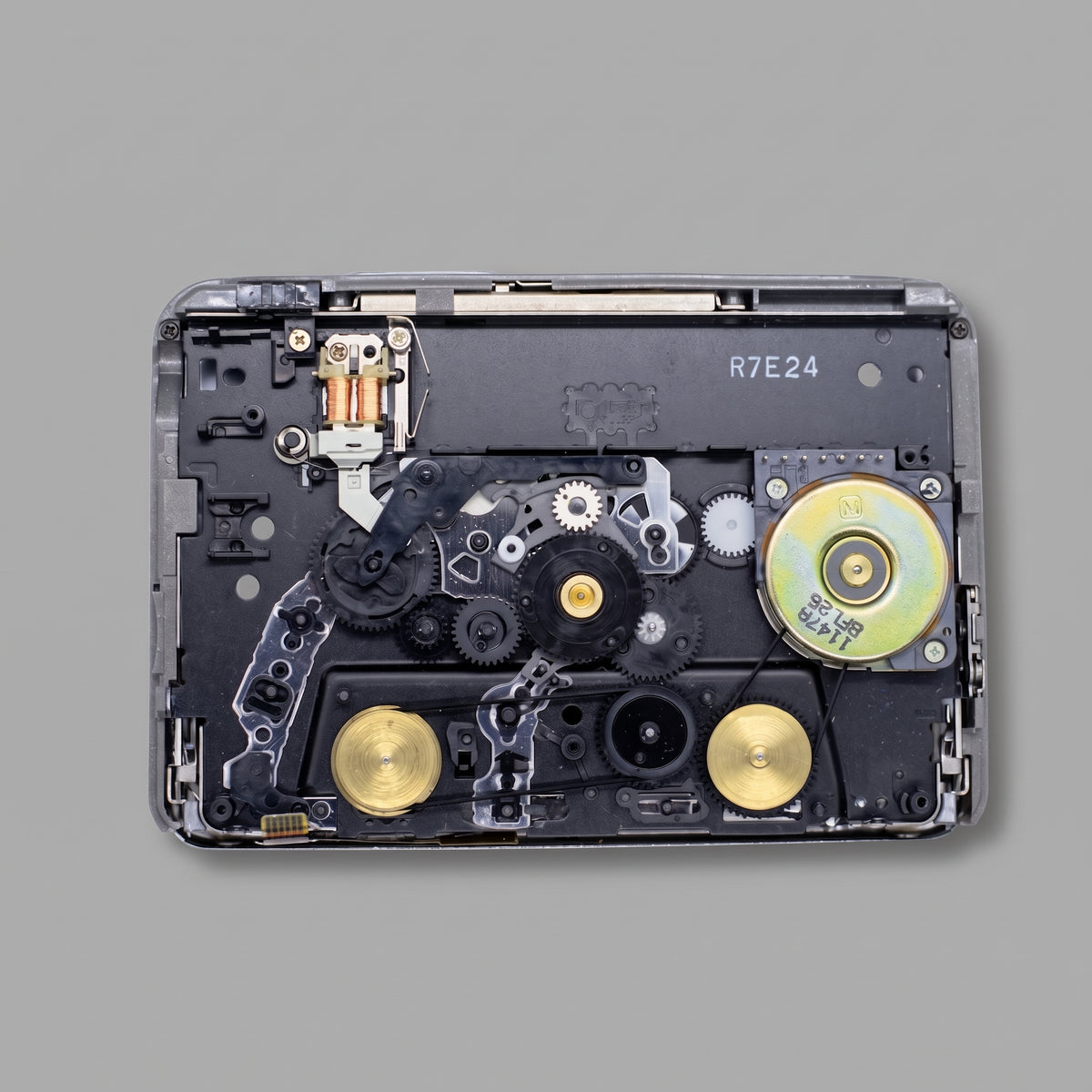 A disassembled electronic device showing internal mechanical components, gears, and metallic parts on a solid gray background.